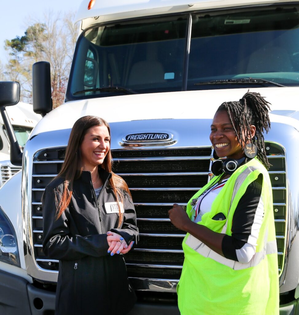 PTP women drivers smiling and talking in front of truck.