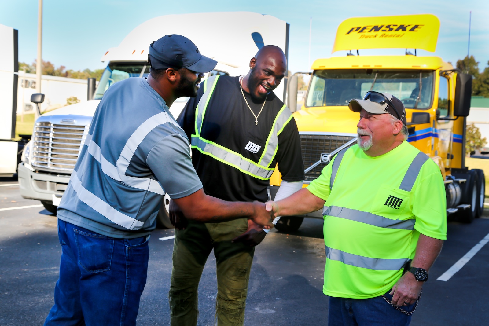 PTP employees (3 men) laughing and shaking hands with truck in background.