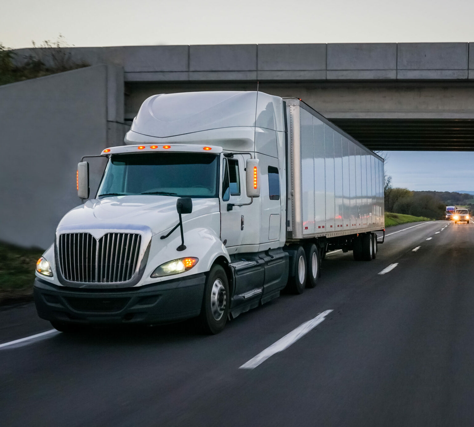 semi tractor trailer driving on the highway in the evening.
