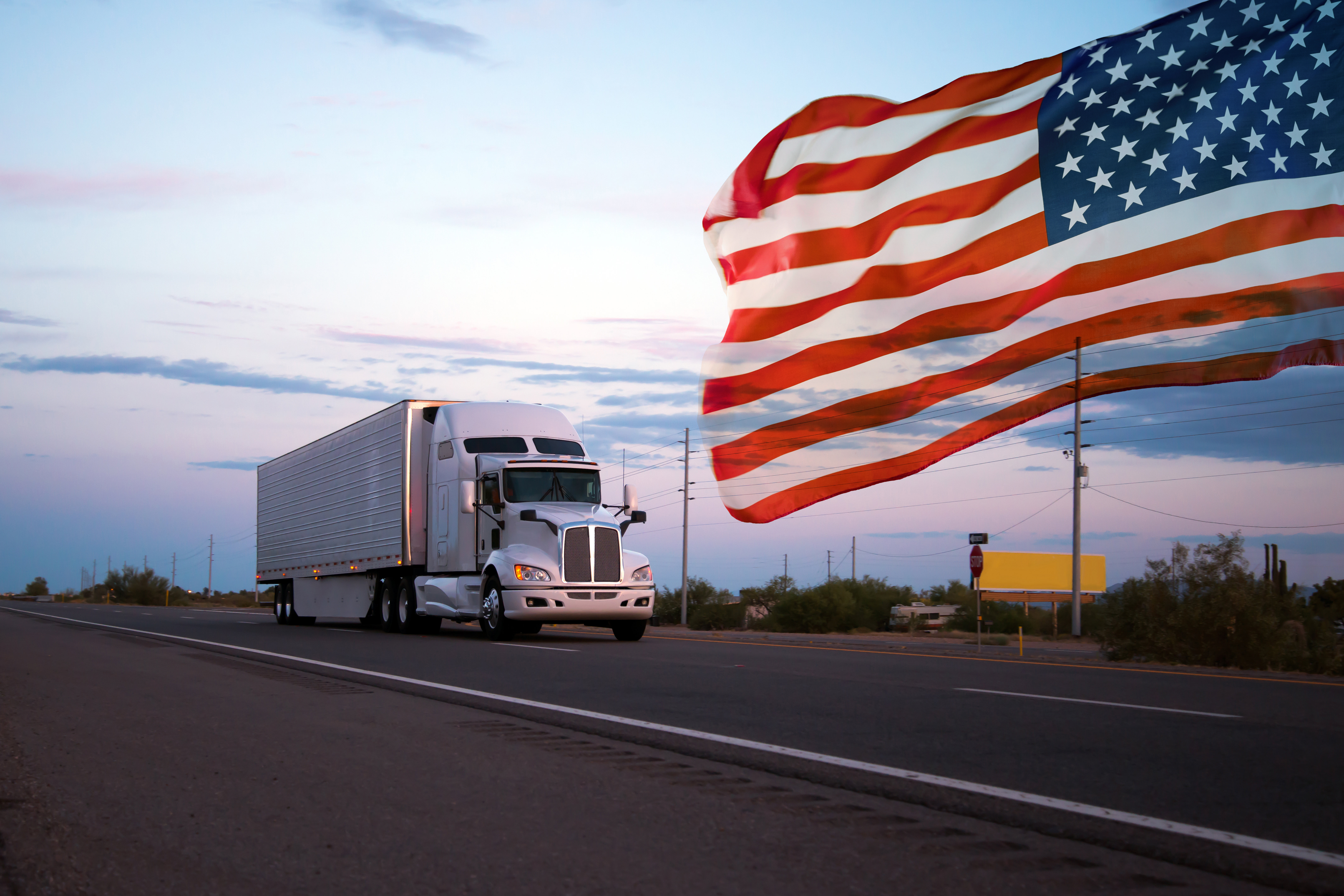 Logistics truck driving on road with american flag waving in the sky